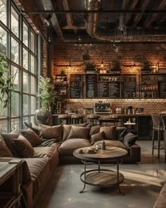 a living room filled with furniture and lots of windows next to a brick wall covered in plants