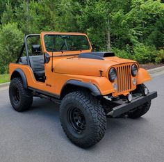 an orange jeep parked on the side of a road in front of some trees and bushes