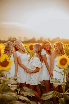 three beautiful young women standing in a sunflower field with one holding the other's hand