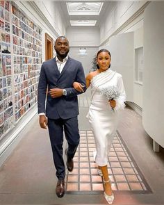 a man and woman are walking down the hallway in front of wall covered with pictures