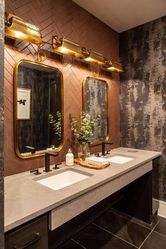 a bathroom with two sinks, mirrors and lights on the wall above them is decorated in black and gold