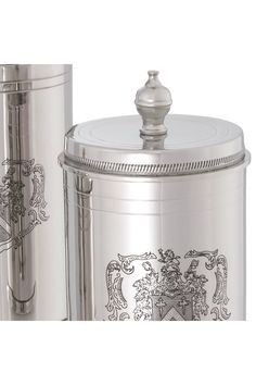 a silver canister with a coat of arms on the front and side, next to it