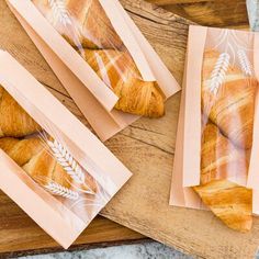 some croissants are wrapped in plastic on a cutting board next to other pastries