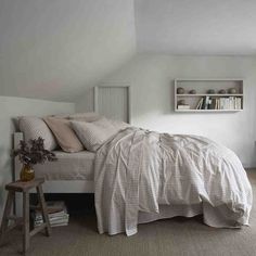 a bed sitting under a window next to a wooden table and book shelf on top of a carpeted floor