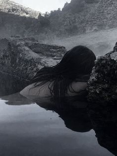 a woman in the water with her hair blowing back and looking at the ground below