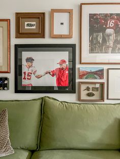 a green couch sitting in front of a wall covered with pictures and framed art on it