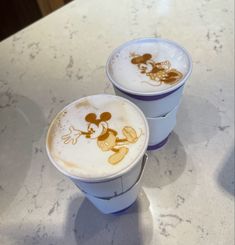 two cups with mickey mouse designs on them sitting on top of a white countertop