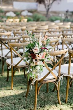 an arrangement of flowers and greenery is arranged on the back of wooden folding chairs