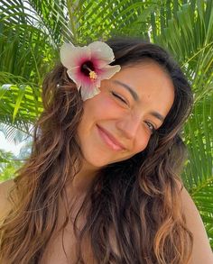 a woman with long hair and a flower in her hair smiles at the camera while standing under palm trees