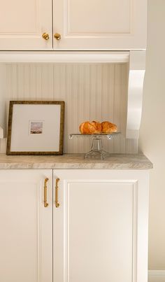 a kitchen with white cabinets and marble counter tops is pictured in this image, there are two croissants on a glass platter