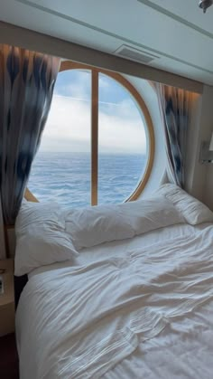 there is a bed with white sheets and pillows in front of a window that looks out to the ocean