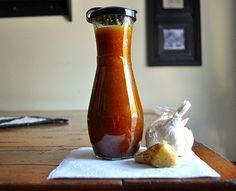 a bottle of sauce sitting on top of a wooden table next to a bag of garlic