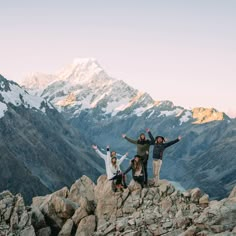 four people standing on top of a mountain with their arms in the air