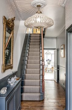 a hallway with stairs, mirror and chandelier