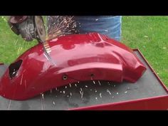 a person using a grinder to cut the hood off of a red car with grass in the background