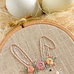 a close up of a cross stitch pattern on a wooden hoop with an egg in the background