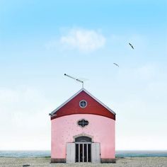 a pink building with a red roof and two birds flying in the sky above it