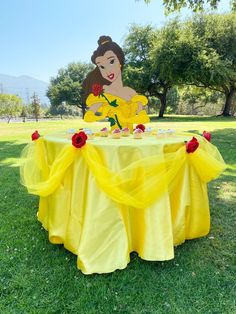 there is a table with a yellow cloth on it and a cake in the shape of a princess