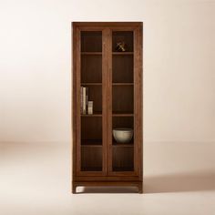 a wooden bookcase with glass doors on the front and bottom shelves, in an empty room