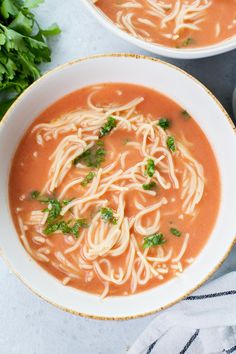 two bowls of soup with noodles and garnishes on the side, next to some parsley