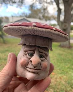 a hand holding up a clay face with a mushroom hat on it's head