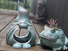 two ceramic frog sculptures sitting on top of a wooden table next to a planter