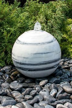 a large white vase sitting on top of a pile of rocks next to some trees