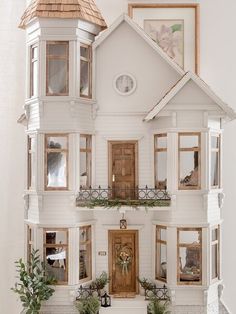 a doll house with lots of windows and plants on the front porch, next to a potted plant