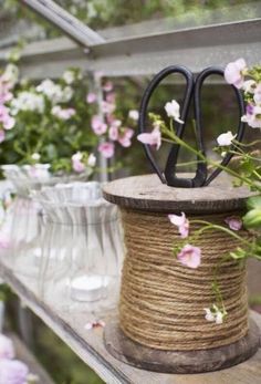 a spool of twine and some pink flowers on a shelf in a greenhouse