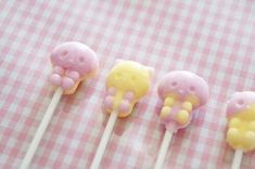 four marshmallows with yellow and pink frosting on a checkered tablecloth