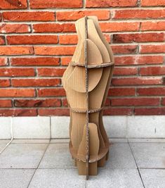 a cardboard sculpture sitting on top of a floor next to a brick wall