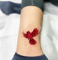 a small red bird tattoo on the ankle is shown in close up, it appears to be flying through the air