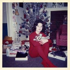 an old photo of a woman sitting in front of a christmas tree with presents on the floor