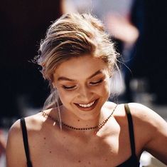 a woman smiling while looking down at her cell phone and wearing a black tank top