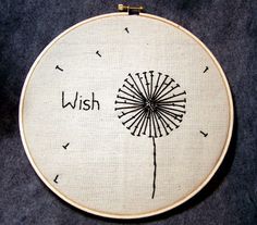 a white embroidery hoop with a dandelion on it and the words wish written in black ink