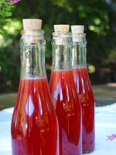 three bottles filled with red liquid sitting on top of a white table cloth next to pink flowers