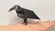 a hand holding a black origami bird on it's left side,