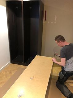 a man standing next to a wooden table in front of black lockers with screwdrivers on them