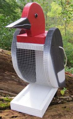 a red and white bird shaped mailbox sitting on top of a wooden log in the woods