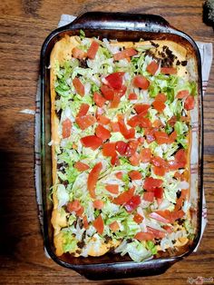 a square pizza with lettuce, tomatoes and other toppings in a casserole dish