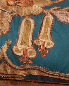 a blue pillow with orange and gold designs on it's sides, sitting on a wooden floor