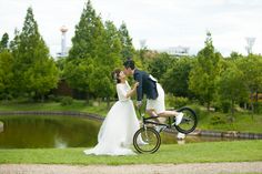 a bride and groom kissing while riding a bike in front of a pond with a water tower in the background