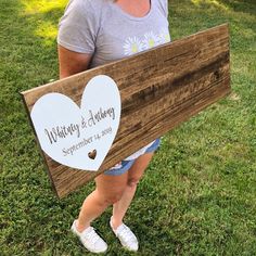 a woman holding a wooden sign with a heart on it that says wedding & anniversary