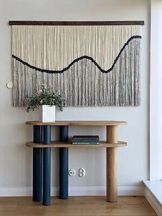 a wall hanging on the side of a white wall next to a wooden table with a plant in it