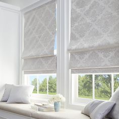 a window with two windows covered in roman shades and white pillows on top of it