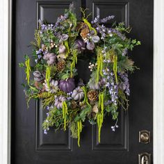 a black door with a wreath on it and purple flowers hanging from the front window