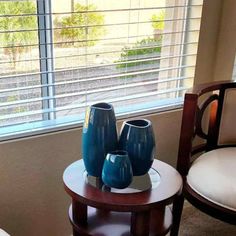 three blue vases sitting on top of a table in front of a window with blinds