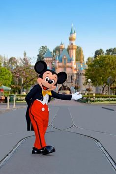 a person dressed as mickey mouse on a skateboard in front of a disney castle