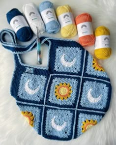 a crocheted bag with yarn and knitting needles on it, next to several balls of yarn