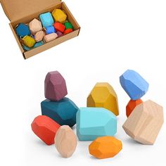 an open cardboard box filled with colorful wooden blocks next to a pile of colored rocks